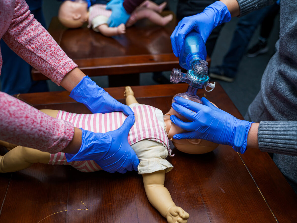 Two people performing baby cpr on a mannequin