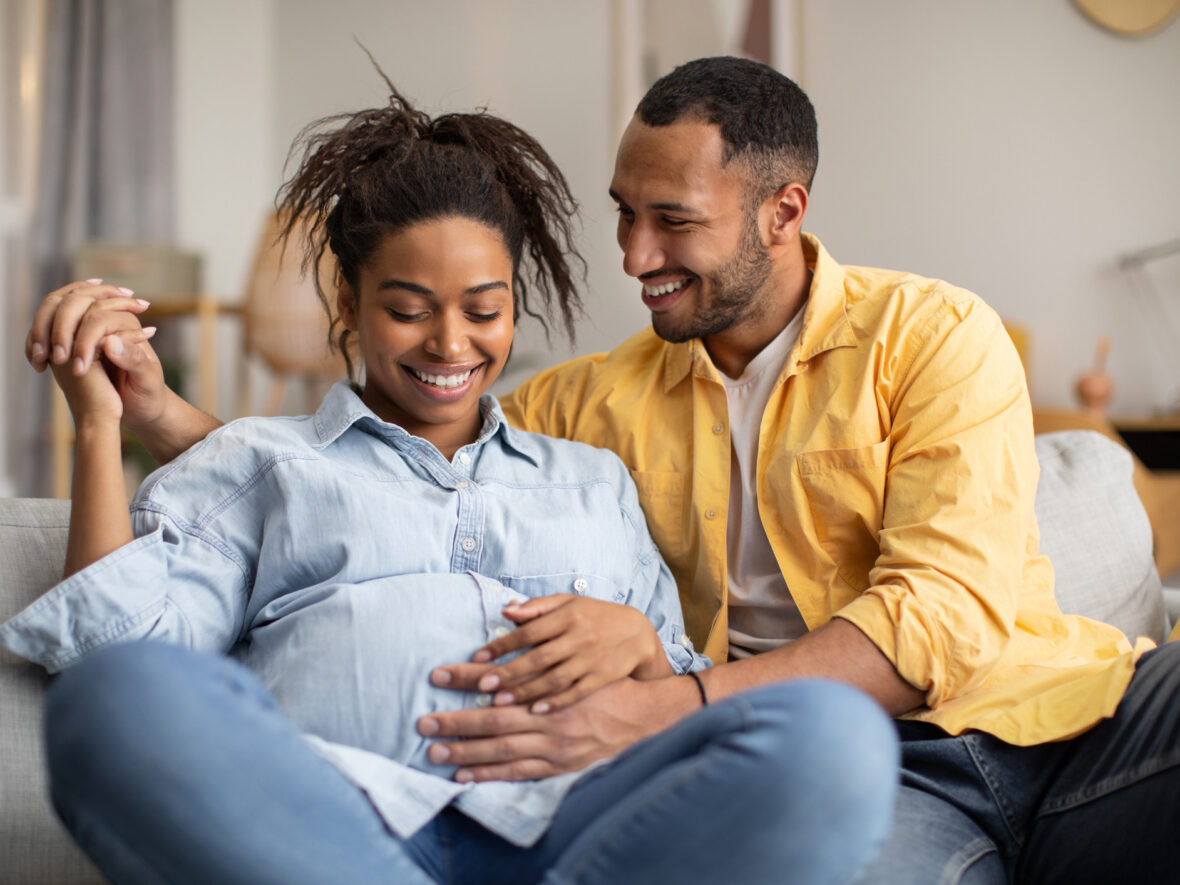 A man sitting beside a pregnant woman, holding her belly