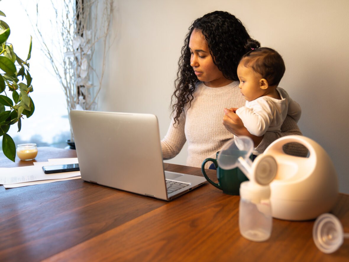 A woman on her laptop holding her baby in one arm