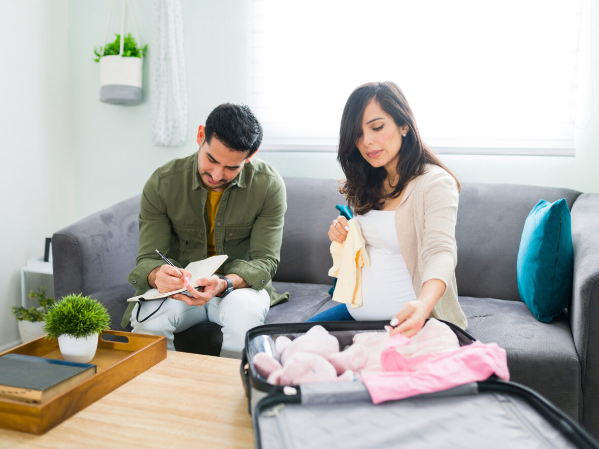 A pregnant woman packing a suitcase in preparation for her delivery date while husband makes list beside her